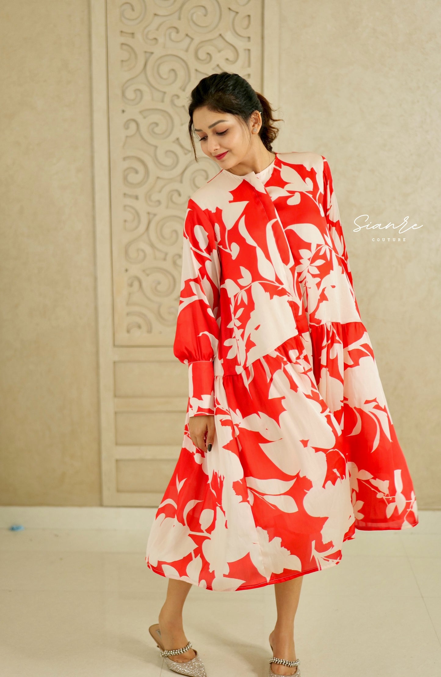 Woman wearing a red and white floral dress against a decorative wall.