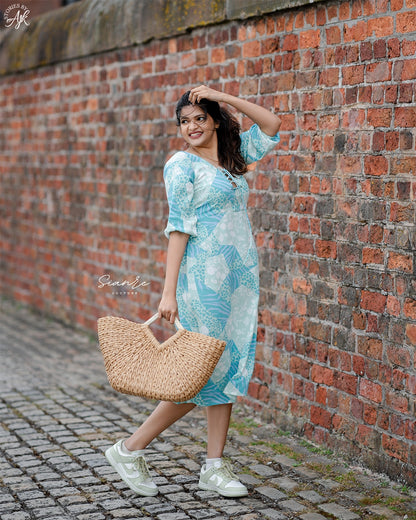 Woman in a blue dress holding a straw bag against a brick wall.