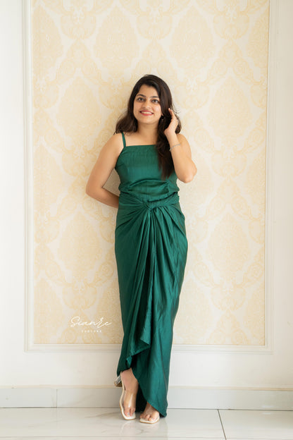 Woman in a green dress standing against a decorative wall.