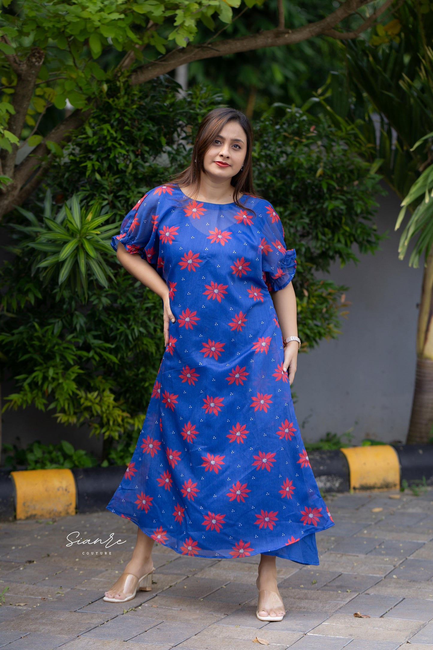 Woman wearing a blue dress with red floral patterns standing outdoors.