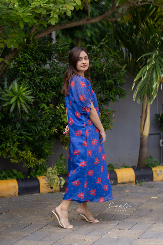 Woman in a blue floral dress standing outdoors with greenery in the background