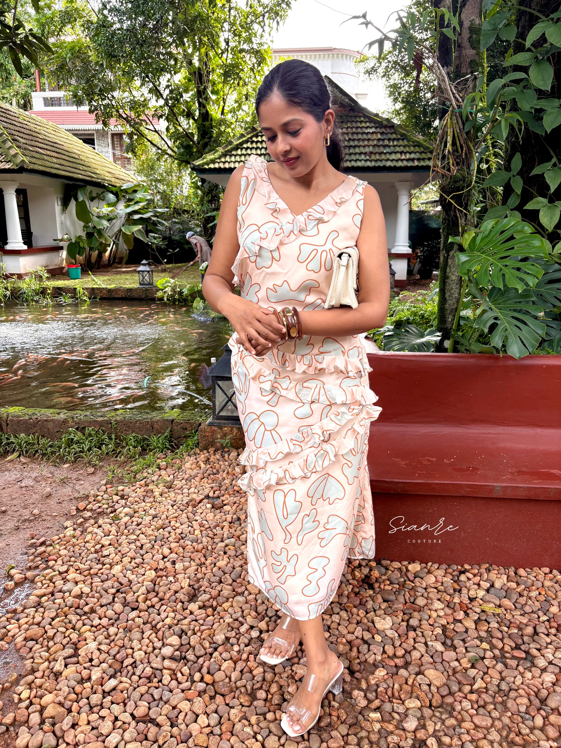 Woman in a floral dress standing outdoors with greenery and a pond in the background