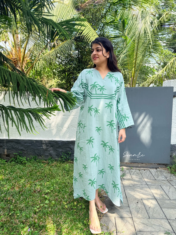 Woman in a light green dress with palm tree pattern standing outdoors near a wall with 'Sunnie' branding.