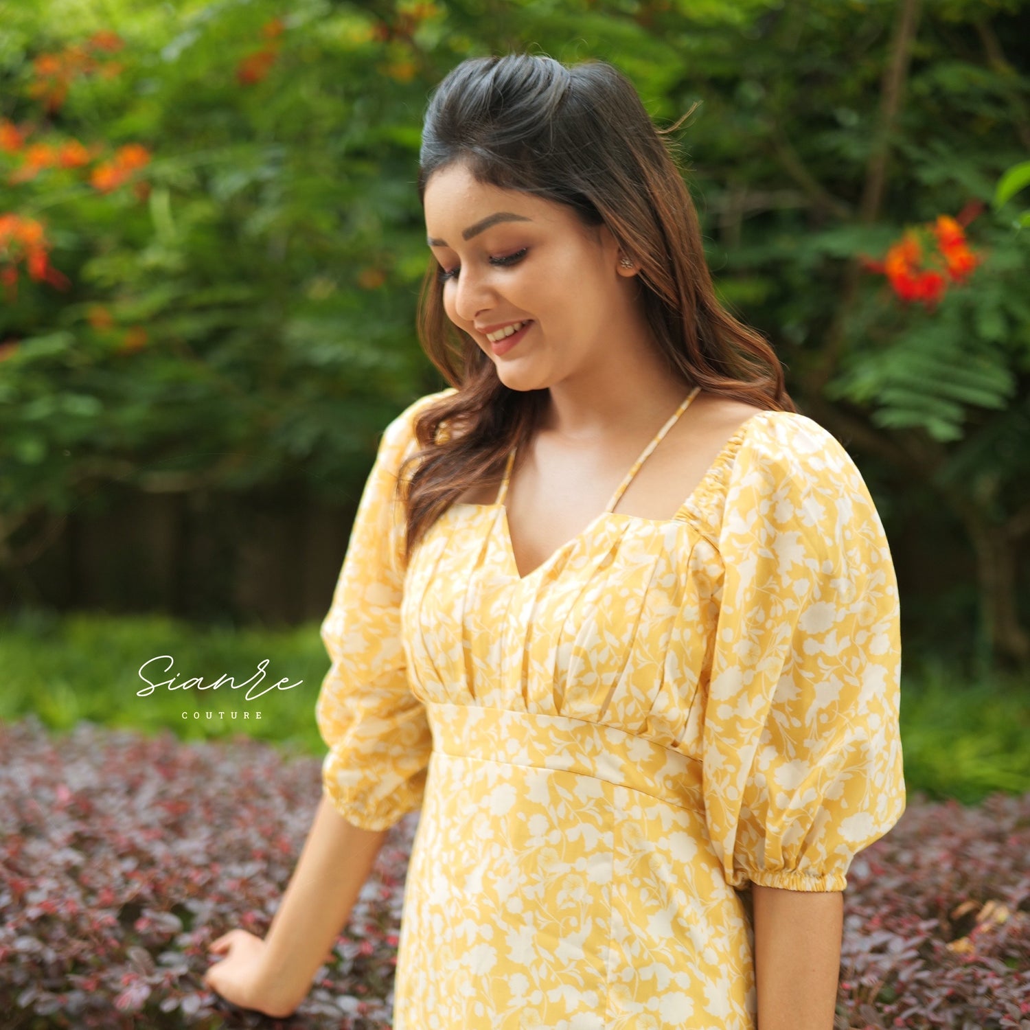 Woman in a yellow dress standing outdoors with greenery in the background