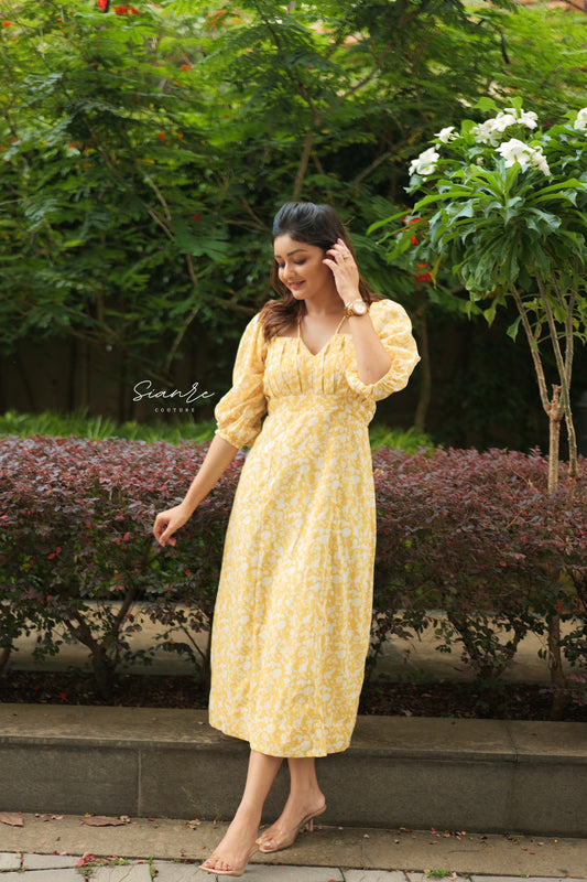 Woman in a yellow dress standing outdoors with greenery in the background