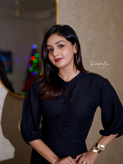 Woman in a black dress standing indoors with a blurred background