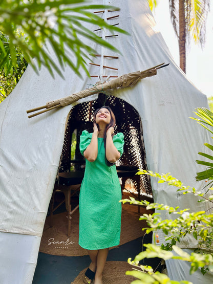 Woman in a green dress standing in front of a white tent with plants around.