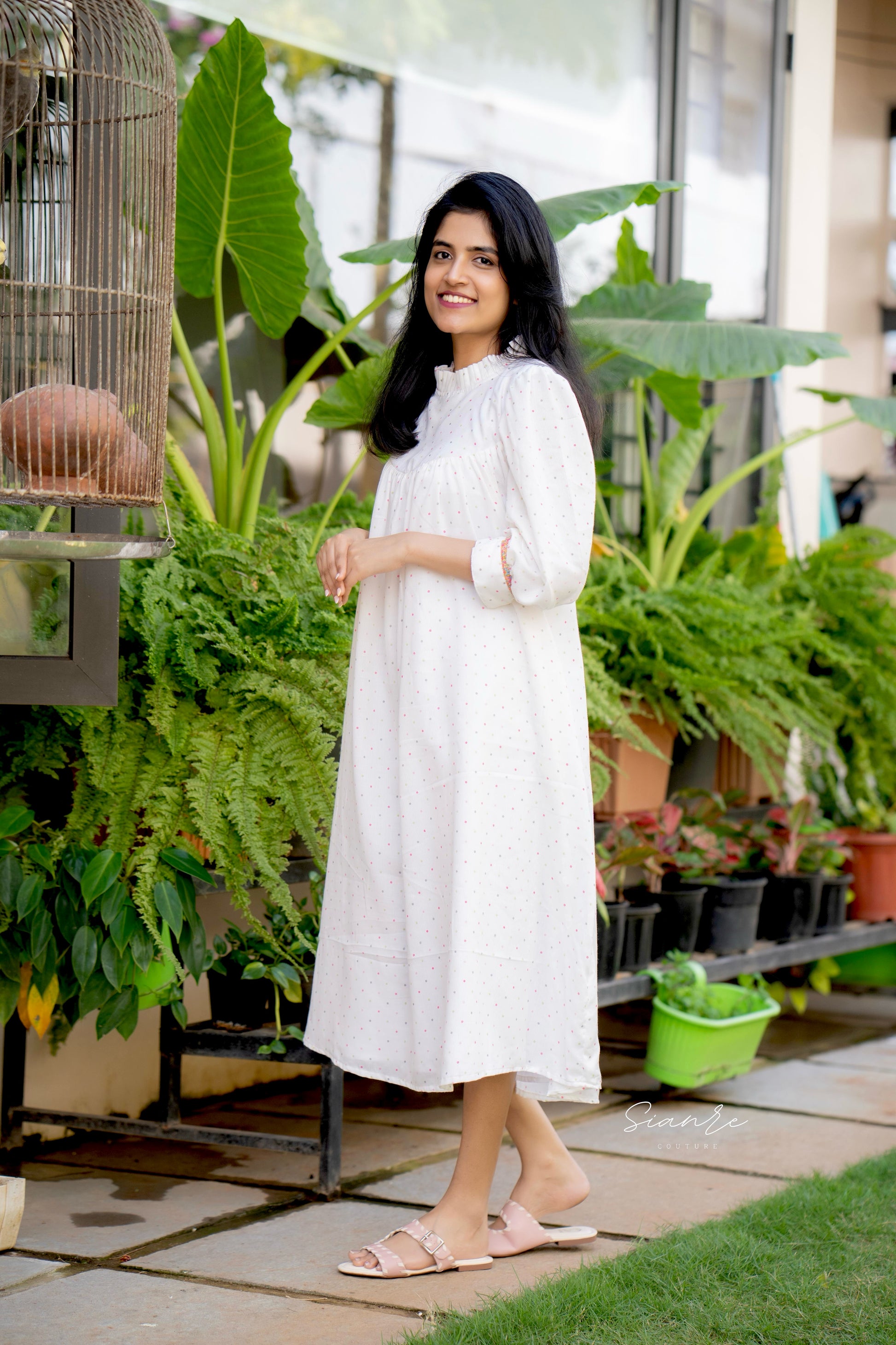 Woman in a white dress standing among plants in an indoor garden setting