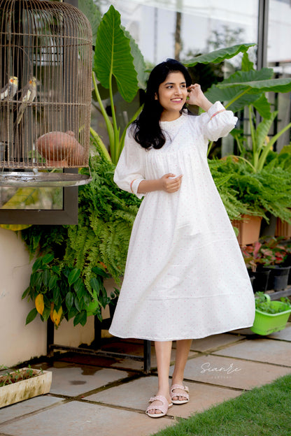 Woman in a white dress standing in a garden with plants and a birdcage.