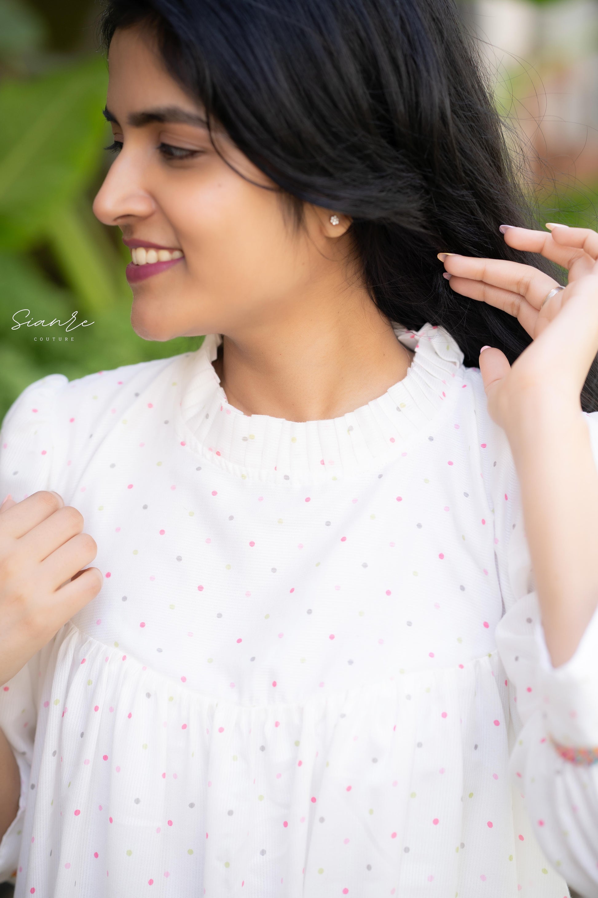Woman in a white outfit with a subtle pattern, holding her hair.