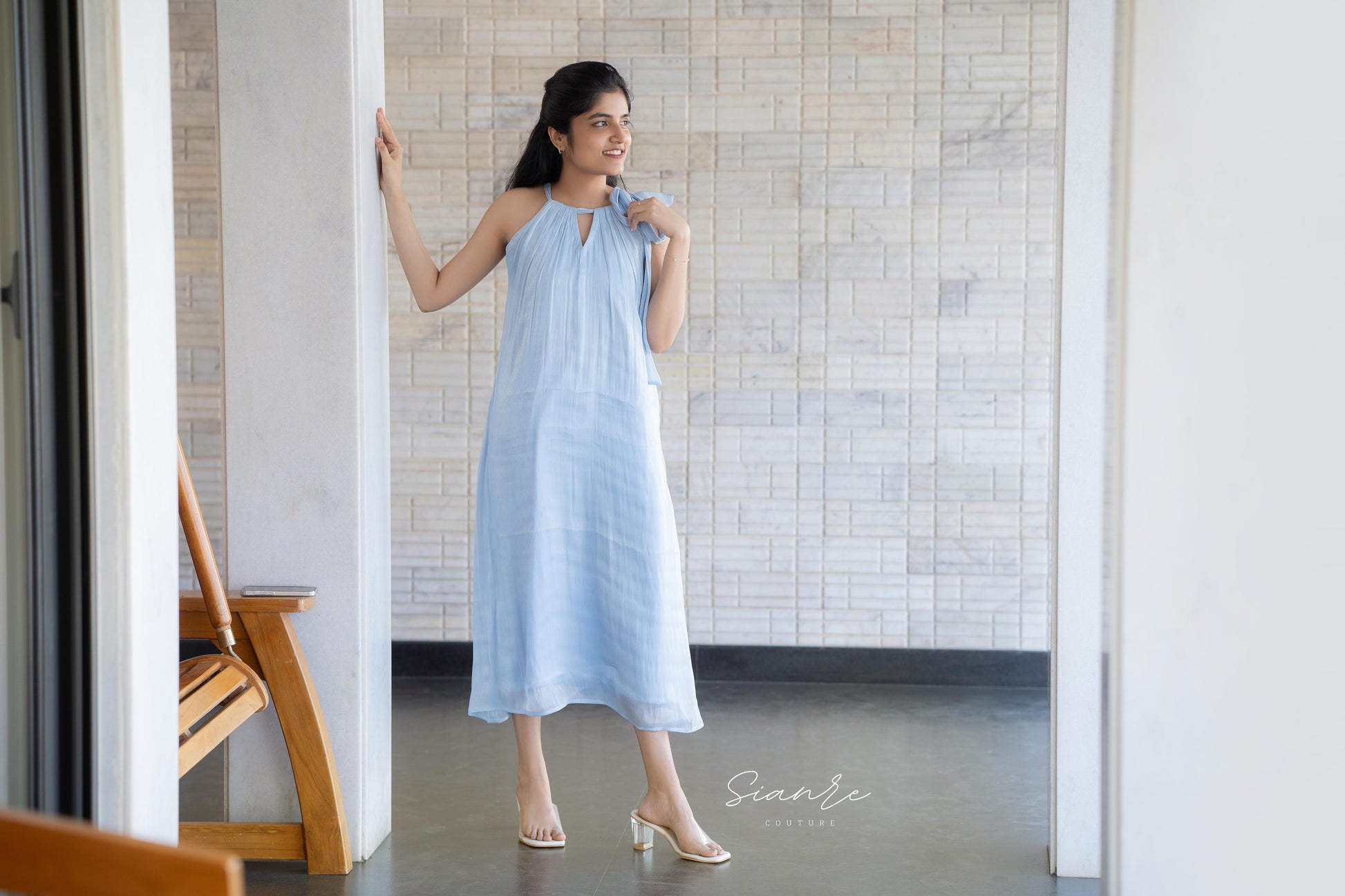 Woman in a light blue dress standing in a room with tiled walls.