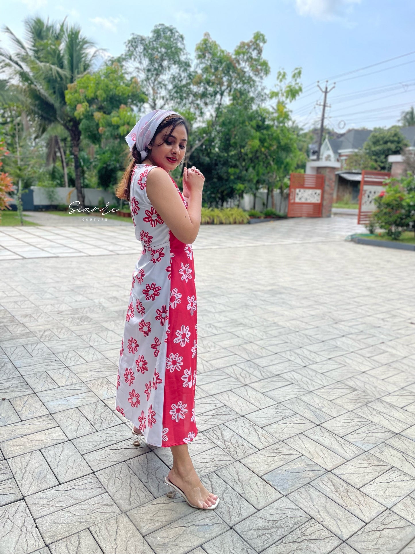 Woman in a floral dress standing on a paved area with greenery in the background