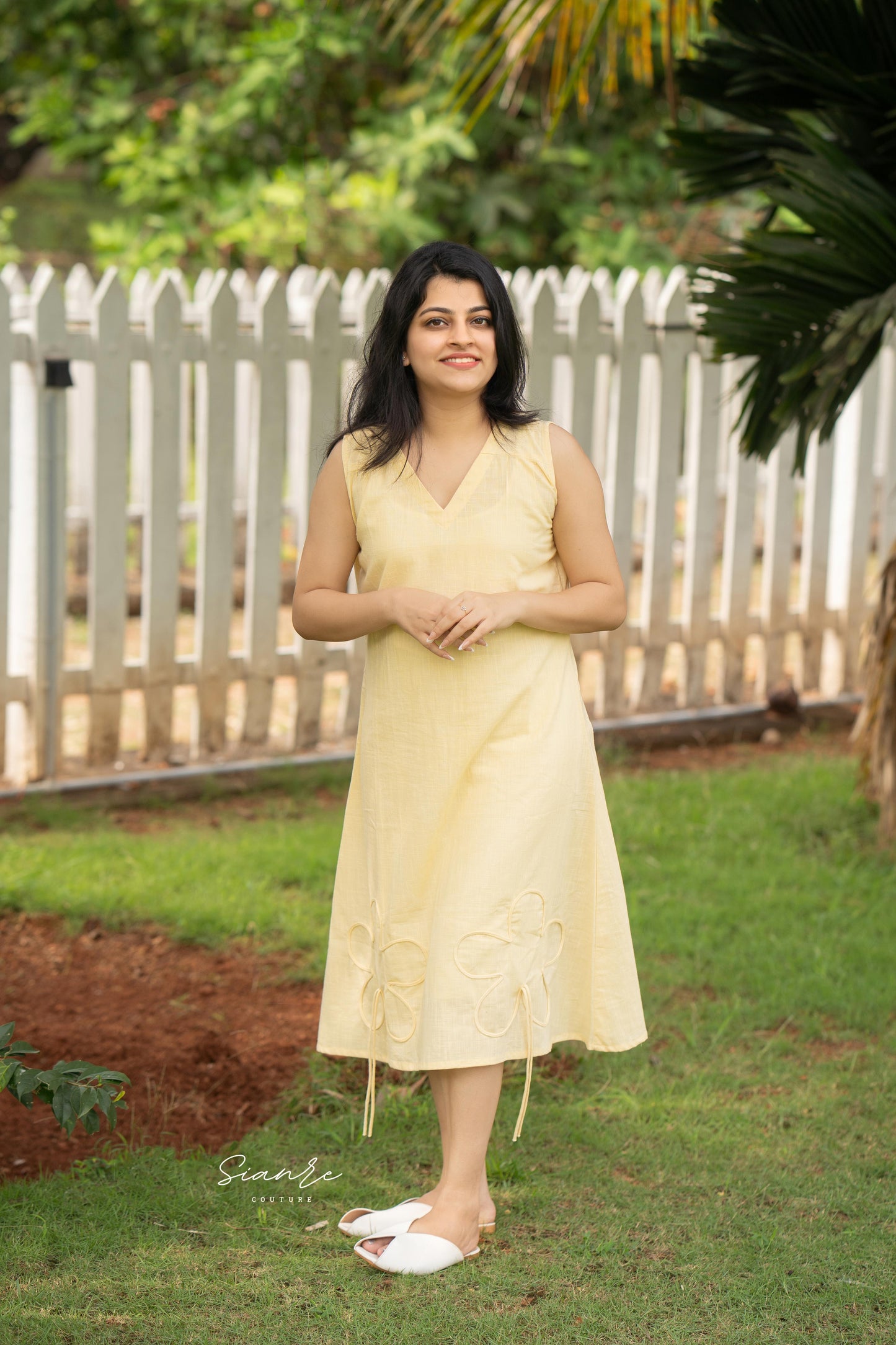 Woman in a yellow dress standing outdoors with greenery in the background