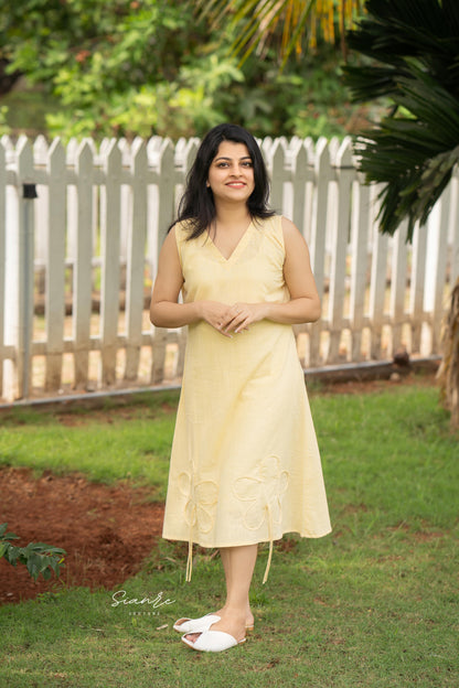 Woman in a yellow dress standing outdoors with greenery in the background