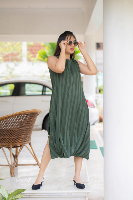 Woman wearing a green dress standing outdoors near a car and a chair.
