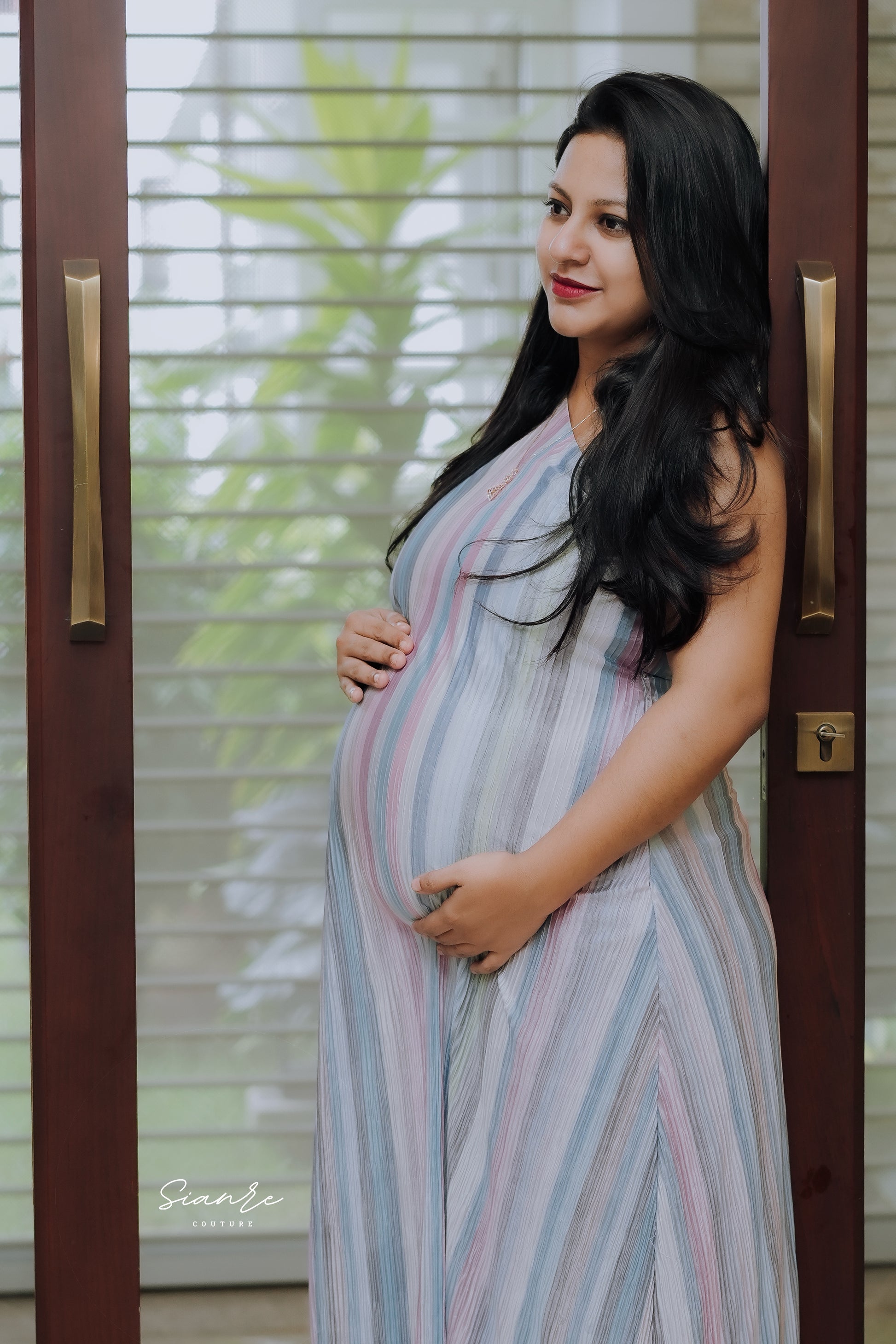 Pregnant woman in a striped dress standing in front of a glass door.