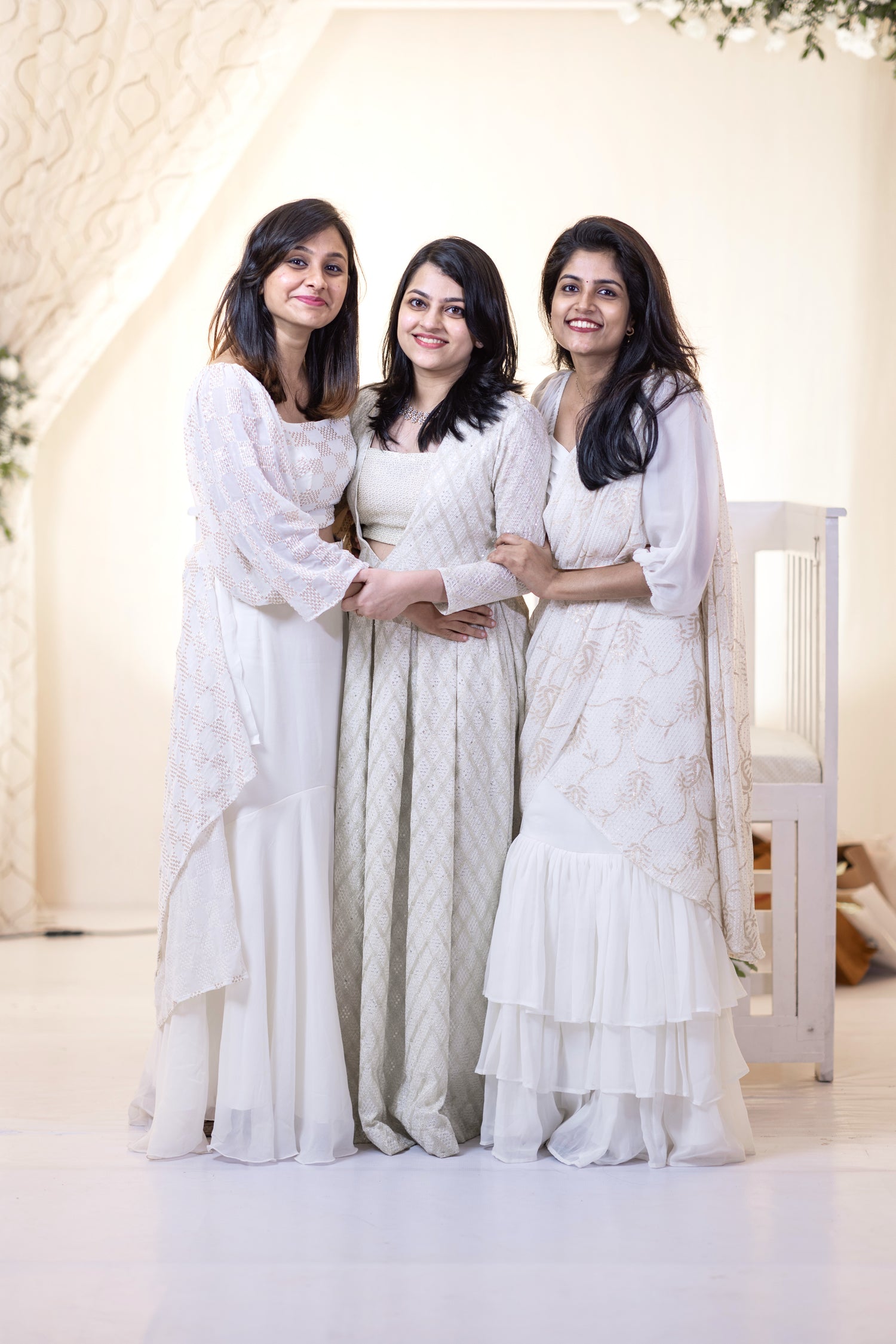 Three women in white traditional outfits standing together in a bright, minimalistic setting.